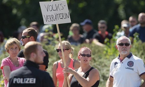 HEIDENAU, GERMANY - AUGUST 26:  An onlooker holds a sign that reads: "Nation Traitor" during a visit by German Chancellor Angela Merkel at the nearby aslyum shelter that was the focus of recent violent protests on August 26, 2015 in Heidenau, Germany. Onlookers standing outside yelled: "Foreigners out!" and "Liar Press" ("Luegenpresse") during Merkel's visit and right-wing demonstrators clashed violently with police last weekend near the shelter. This is Merkel's first visit to a shelter for migrants seeking asylum in Germany. Germany is expecting to receive at least 800,000 migrants and refugees this year and the country has seen a spate of protests, arson attacks and violence by right-wing protesters opposed to the arrival of the migrants in recent weeks.  (Photo by Sean Gallup/Getty Images)